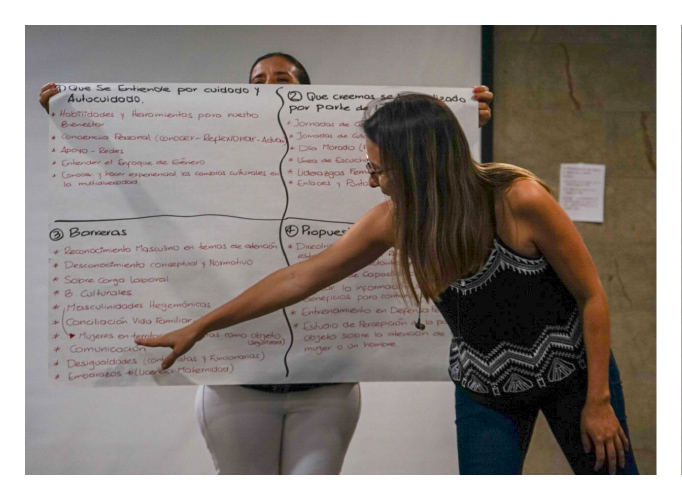 Dos mujeres, una sosteniendo una cartelera, la otra explicando el contenido de la misma