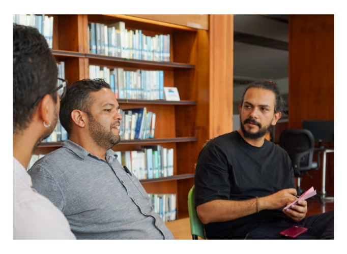 Tres hombres, uno de ellos está hablando, los dos están atendiendo lo que está hablando