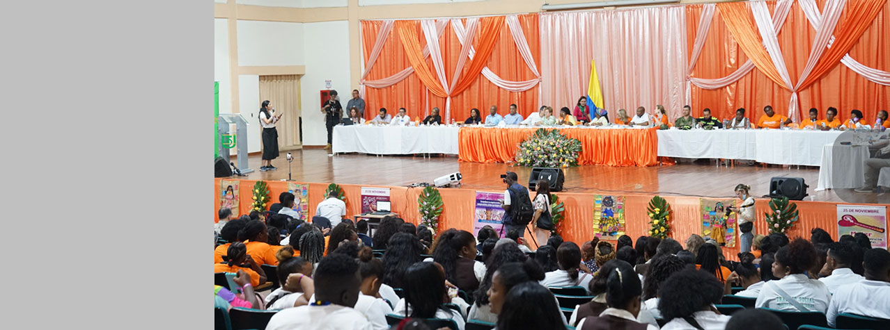Foto desde la parte de atrás de un auditorio donde hay muchas personas y en el fondo se ve una mesa  con 25 personas 