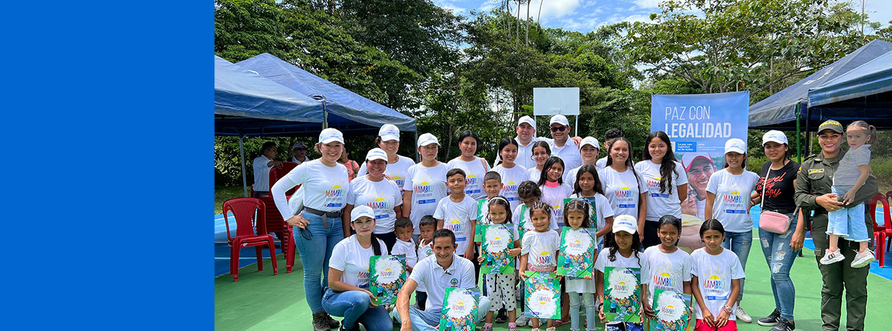 Grupo de personas hombres mujeres, niños y niñas posando para una foto con un diploma que dice Mambrú  
