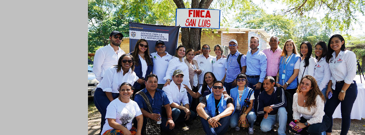 Grupo de 23 personas hombres y mujeres posando para una foto y detras hay un letrero que dice finca San Luis