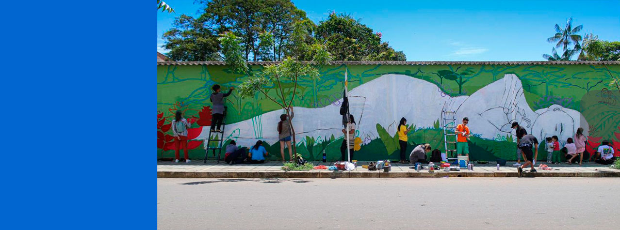adultos y niños pintando un mural de una mujer acostada en la hierva 