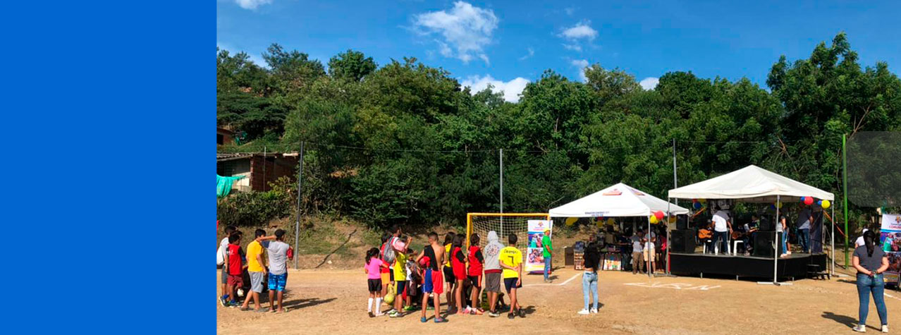 Foto de cancha de futbol con personas  y 2 carpas de una de ellas con una tarina y sobre ella personas con instrumentos musical