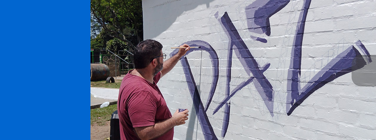 Foto de un Hombre dibujando un mural con un pincel Excribiendo la palabra paz en color morado