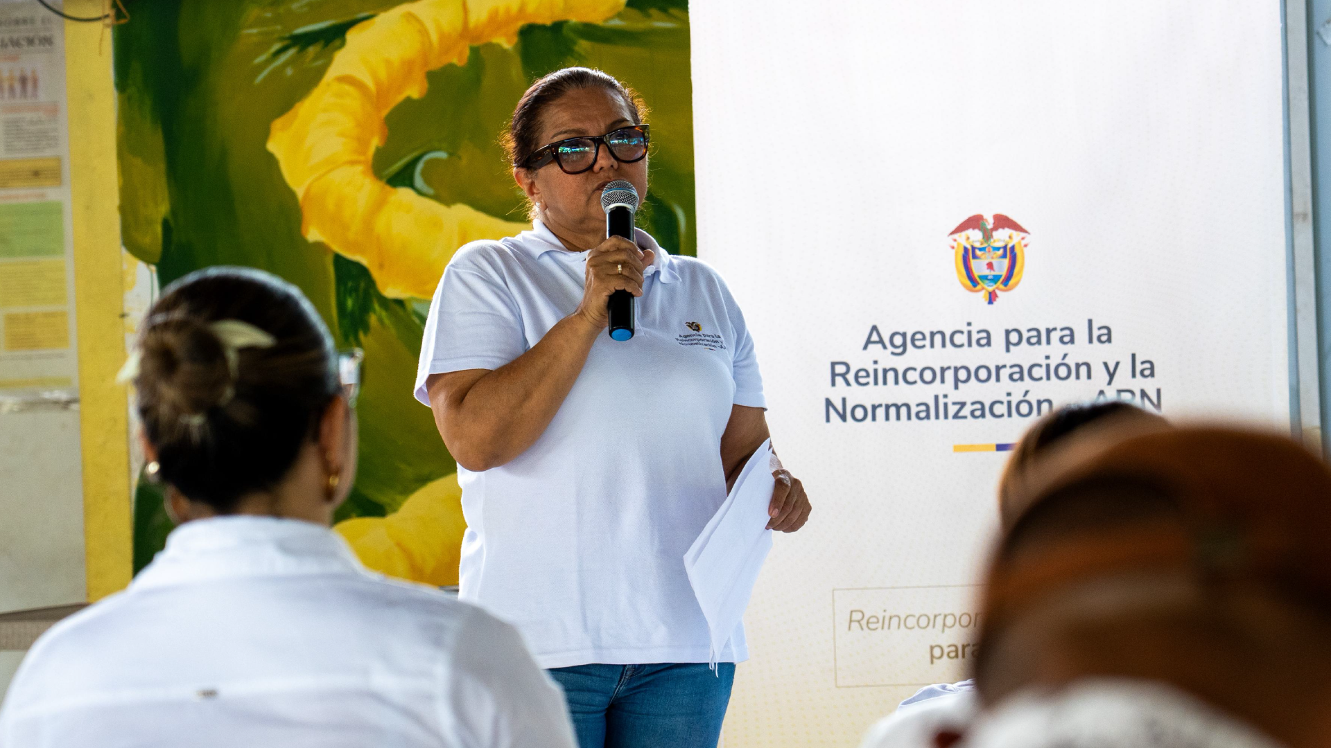 mujer hablando al frente de un público con micrófono