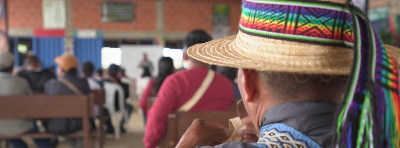 Al fondo se ve un grupo de gente reunida, escuchando a una señora. Al frente se ve un señor con un gorro.