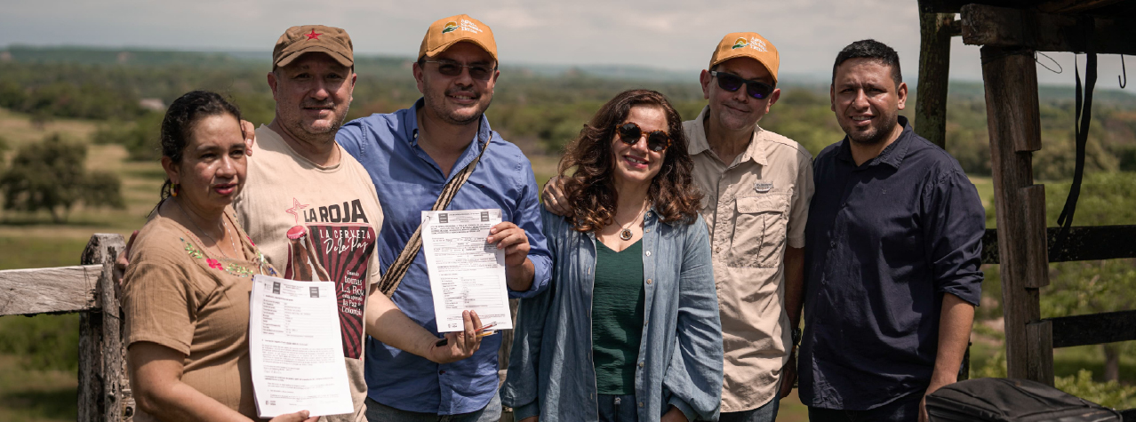Grupo de personas sonrientes, dos de ellas mostrando unos documentos