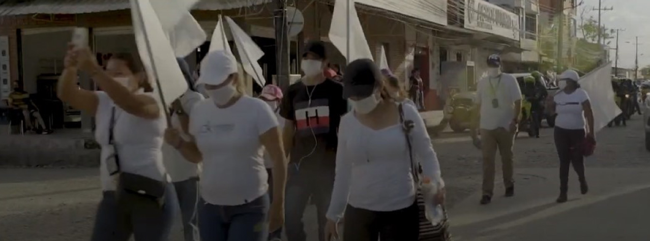 personas caminando por la calle, con tapabocas puesto y llevando banderas blancas