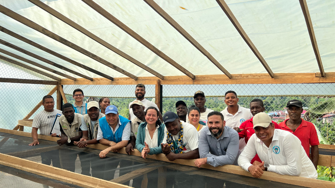 Firmantes de paz, campesinos y representantes institucionales posan en una infraestructura para producción de cacao