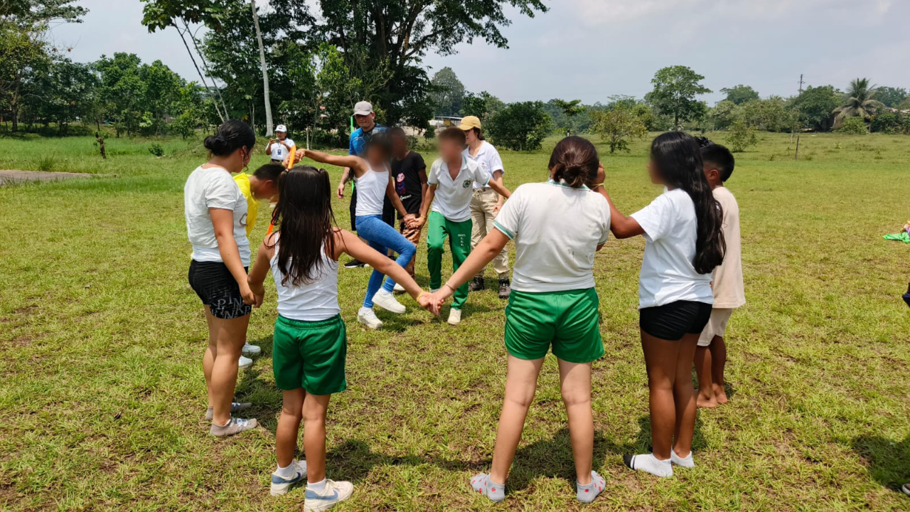 Niños y niñas realizan actividades lúdicas al aire libre en una zona verde en espacio de integración comunitaria.
