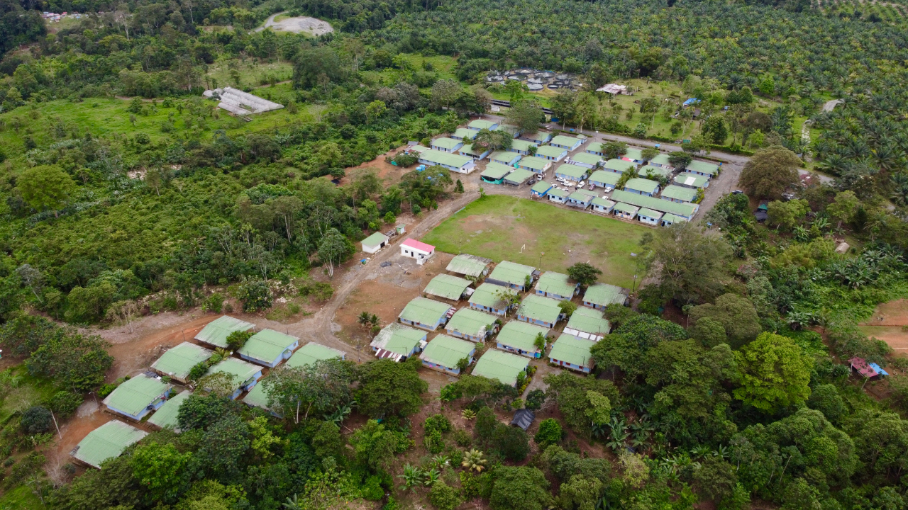 Vista aérea de comunidad rural en proceso de reincorporación en Colombia rodeada de bosque.