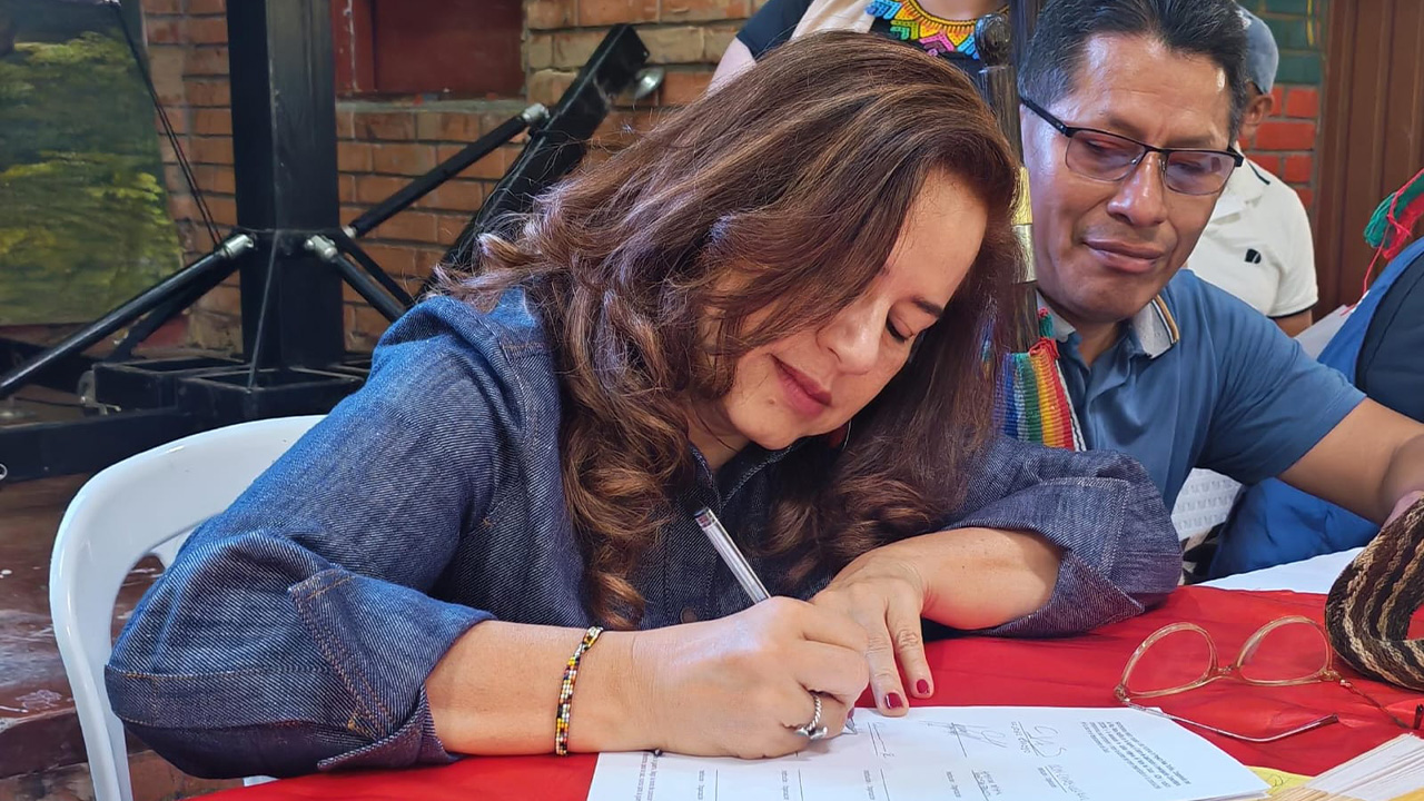 Alejandra Miller firma un documento durante un evento institucional